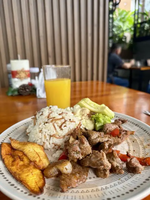 Plato de carne con arroz, maduros, aguacate y jugo de naranja