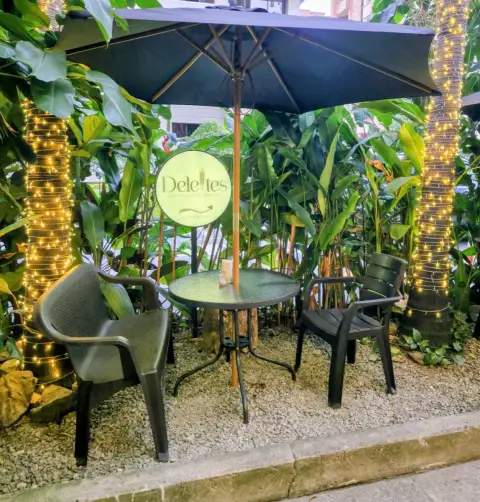 Mesa en el jardín de Deleites, con sombrilla, plantas y luces